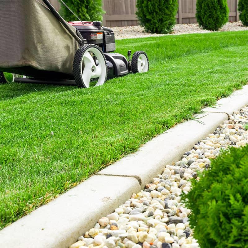 Lawn maintenance beside concrete landscape curbing and planting bed edging in a residential yard